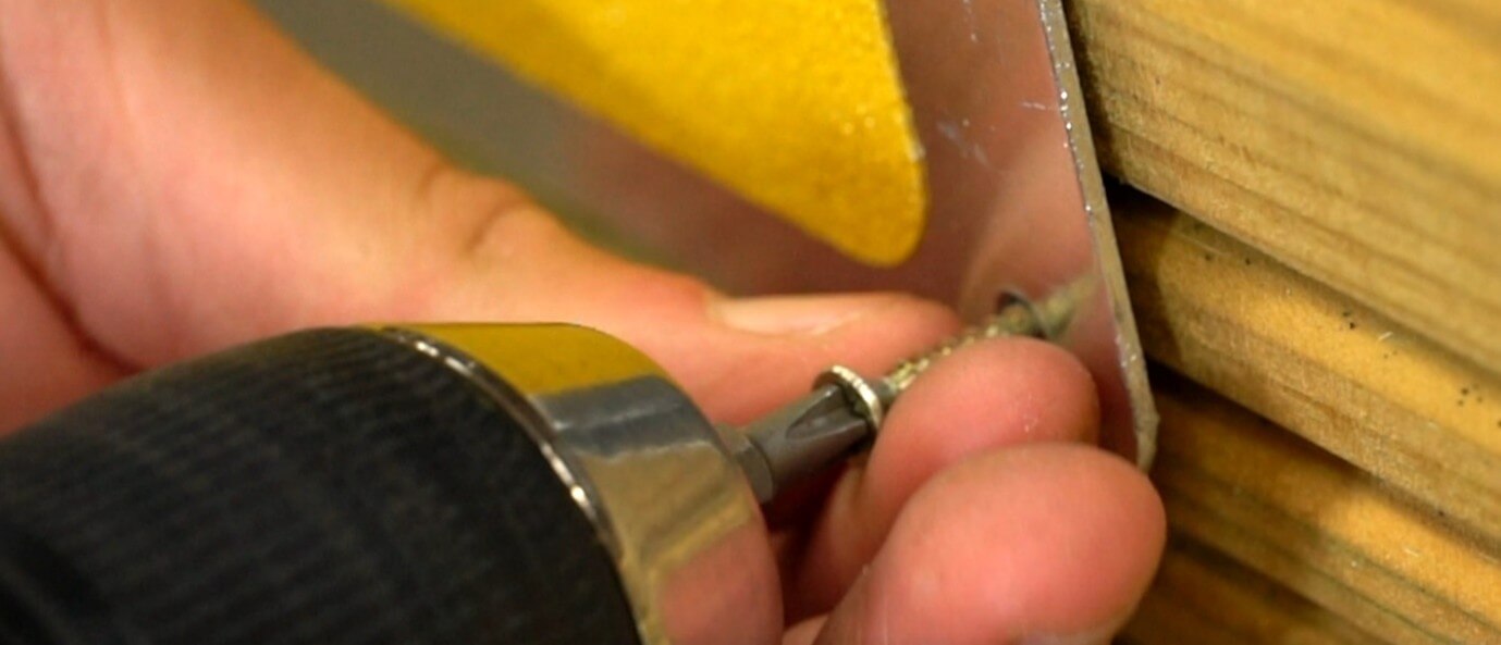 A person holding a drill close-up to drill holes into the wood for the anti-slip plates.